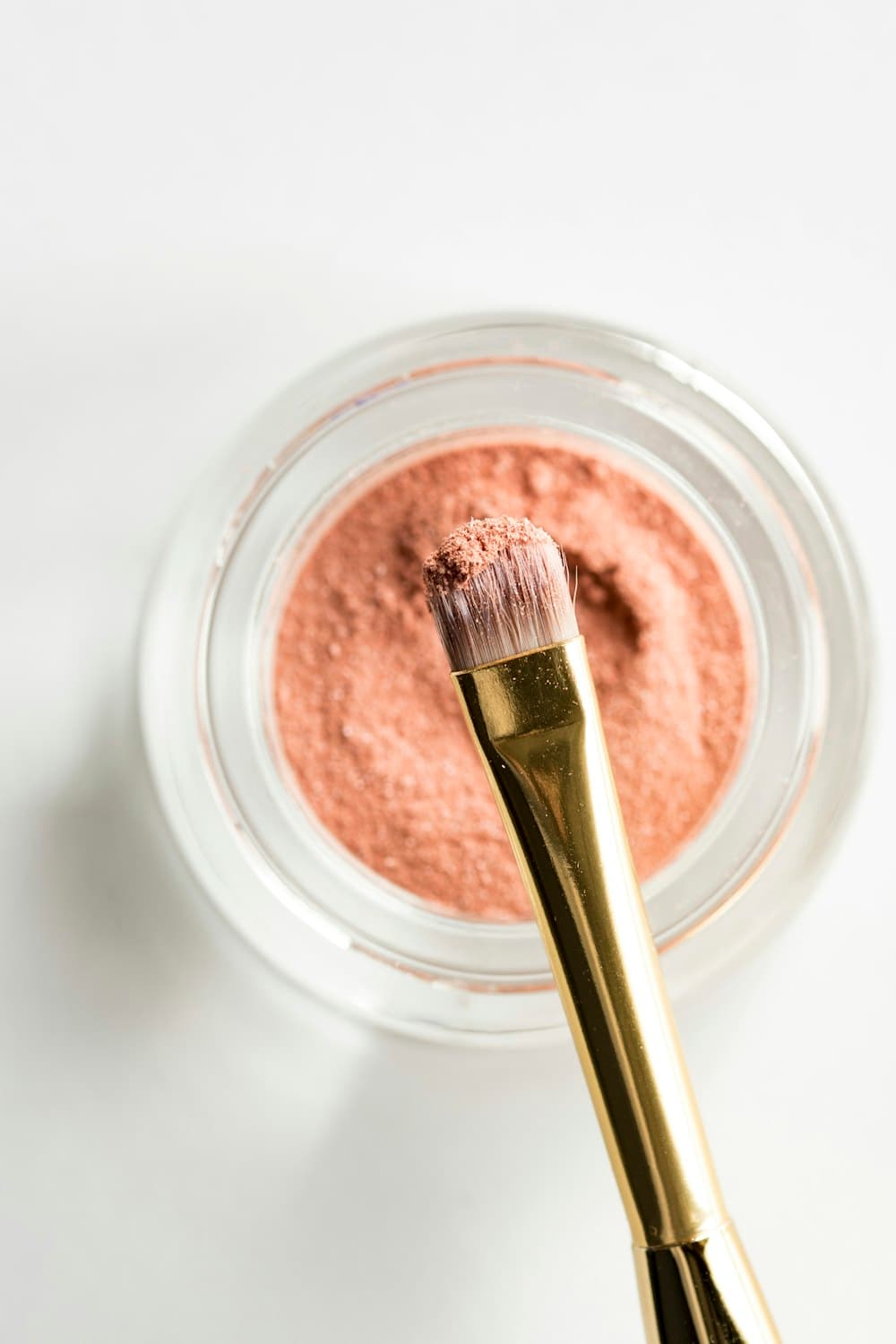 A pink makeup brush resting in loose blush powder