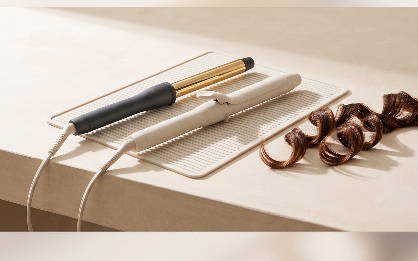 Unbranded curling irons and a wavy hair swatch on a cream surface